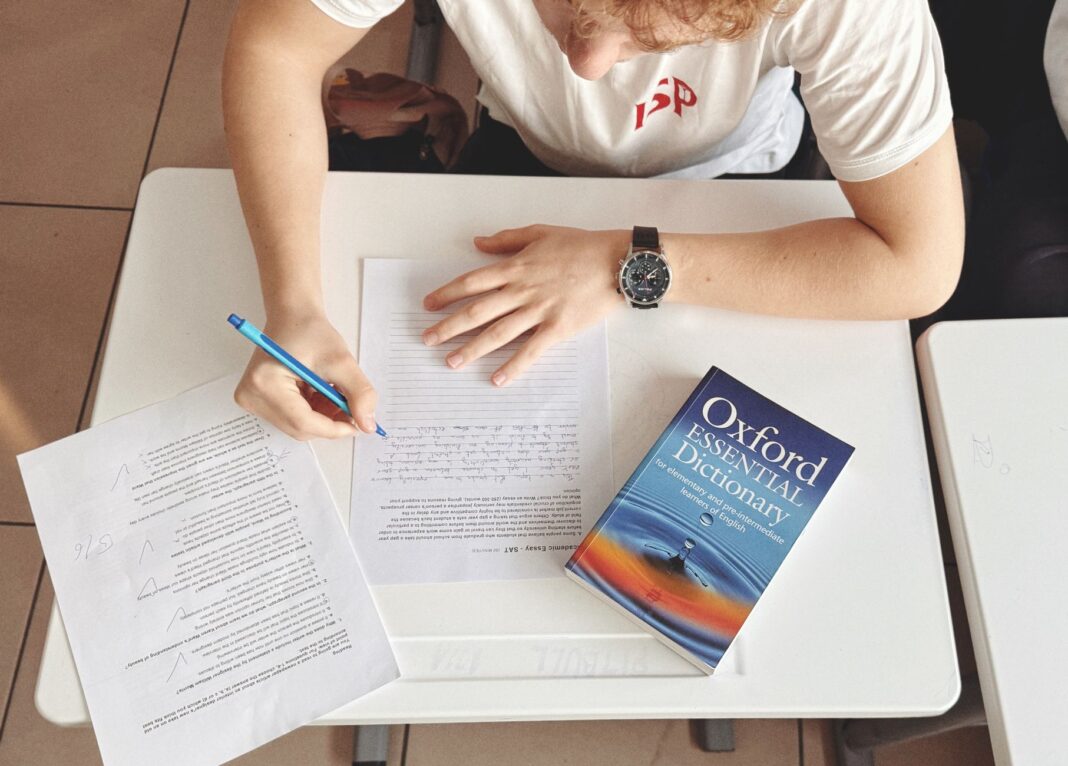 Student pisze test przy biurku z papierem i słownikiem Oxford Student pisze test przy biurku z papierem i słownikiem Oxford